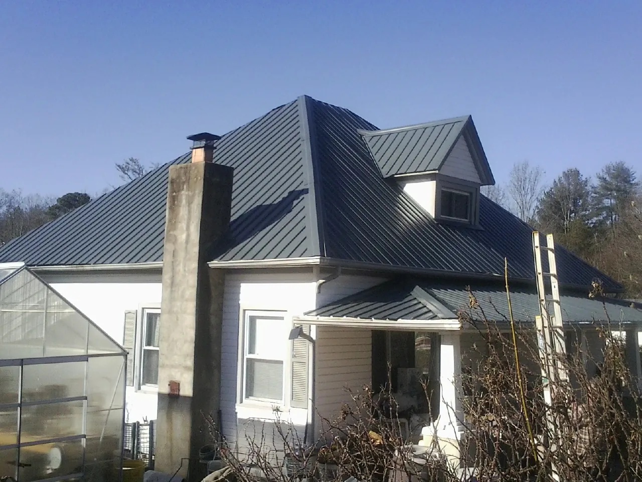 Dark blue standing seam metal roof on a white farmhouse with dormer — Slate & Tile Roof Repair by Roofing Brothers in Indianola