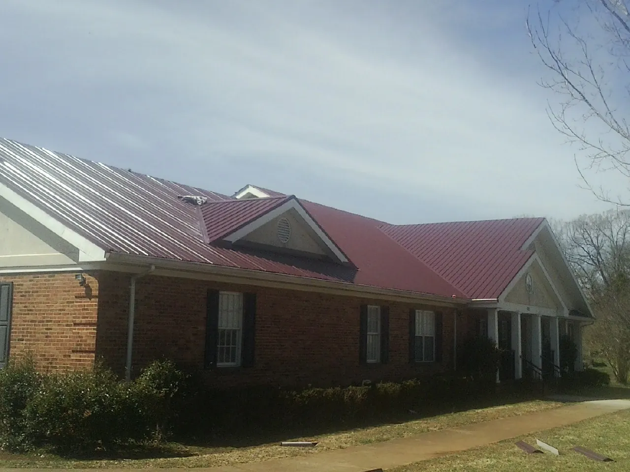 Red metal roof with gabled entries on a long brick building, from a Hail Damage Roof Repair job in Indianola