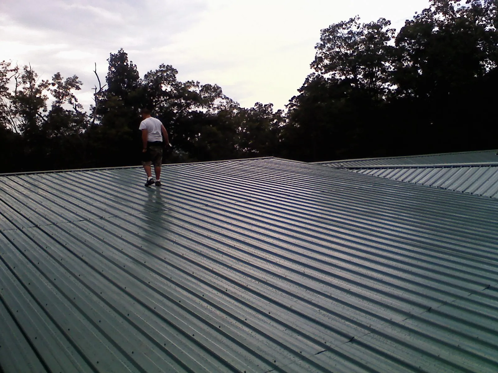 Roofer walking a wide expanse of new green metal roofing in Indianola